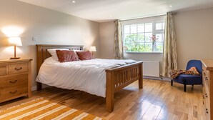 Een slaapkamer met een houten bed, nachtkastje, stoel en raam met gordijnen.