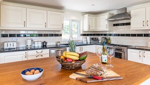 Een moderne keuken met witte kasten, een houten aanrecht, een mand met fruit, een snijplank met brood en een wijnglas.