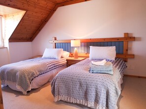 A room with two beds, wooden headboards, and a sloped ceiling.
