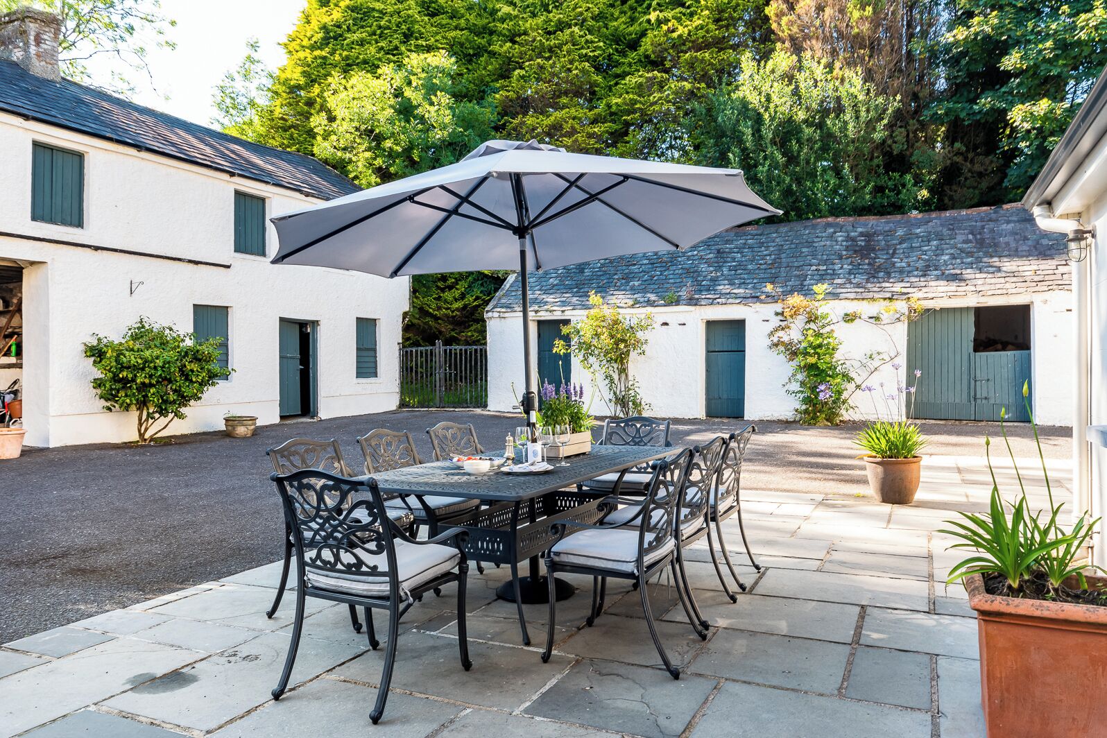 An outdoor patio with a round table and chairs, a large umbrella, and potted plants.