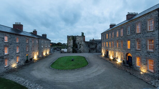 A courtyard with stone buildings, a grassy area, and a castle-like structure in the background. - 4 bed Historically Significant House Sleeping 8 (Ennis)