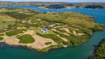 An aerial view of a coastal area with a small settlement, green fields, and a body of water.