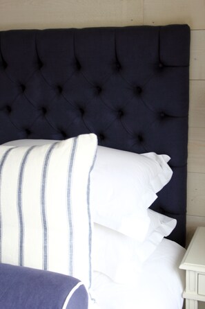A bed with a dark tufted headboard and white pillows with blue stripes.