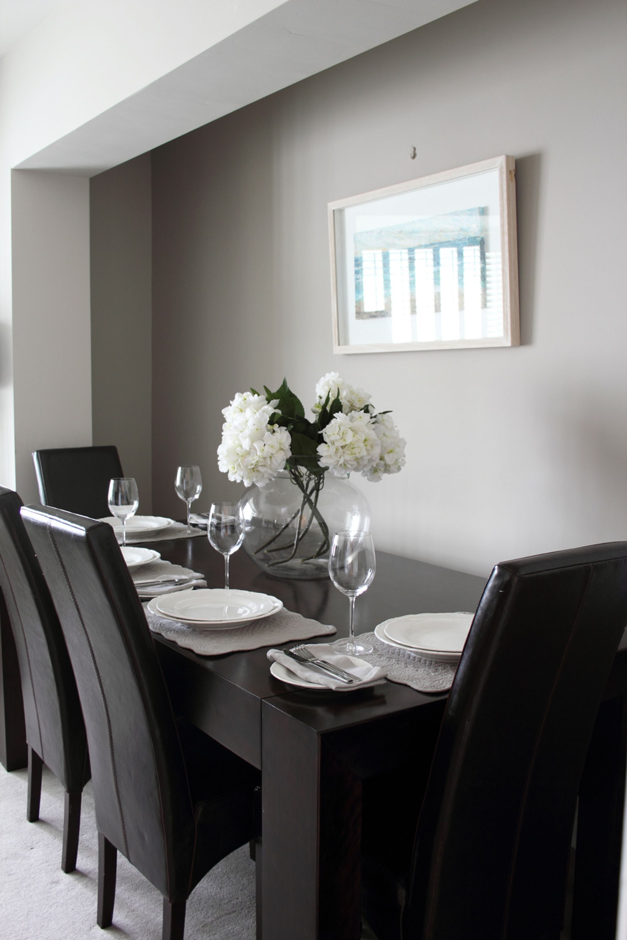 A dining area with a dark wooden table set for four, white plates, and a vase with white flowers.