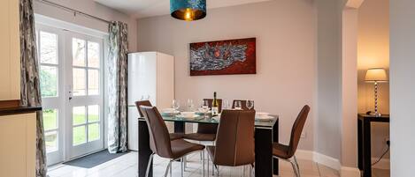 A dining area with a table set for four, chairs, a modern pendant light, and a painting on the wall.