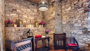 Quarto com paredes de pedra, móveis de madeira, um candelabro, velas e flores.
