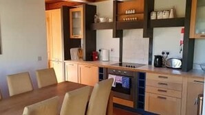 A dining area with a wooden table and chairs, a kitchen with a stove, cabinets, and a sink. - 4 Bedroomed House in Waterville Close to the Beach (Waterville)