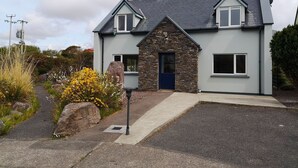 A two-story house with a stone facade, a blue door, and a grey roof. - 4 Bedroomed House in Waterville Close to the Beach (Waterville)