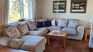 A living room with a sectional sofa, a coffee table, and a window with curtains. - 4 Bedroomed House in Waterville Close to the Beach (Waterville)