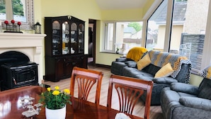Un salon avec une cheminée, une table à manger avec des chaises, un canapé et une grande fenêtre.