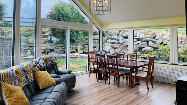 Un intérieur moderne avec un coin repas, de grandes fenêtres et un mur en pierre à l’extérieur.