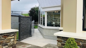 Un étroit sentier mène à une maison aux murs de pierre, avec une fenêtre donnant sur un jardin.