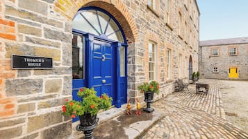 A historic stone building with a blue door, a sign reading 'Thomond House,' and a cobblestone courtyard with benches and potted plants.