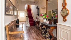 A grand hallway with a wooden bench, a staircase with red carpeting, a large mirror, and a wall-mounted clock. - Beautifully Restored Soldier s Barracks to Sleep 10 People (Ennis)