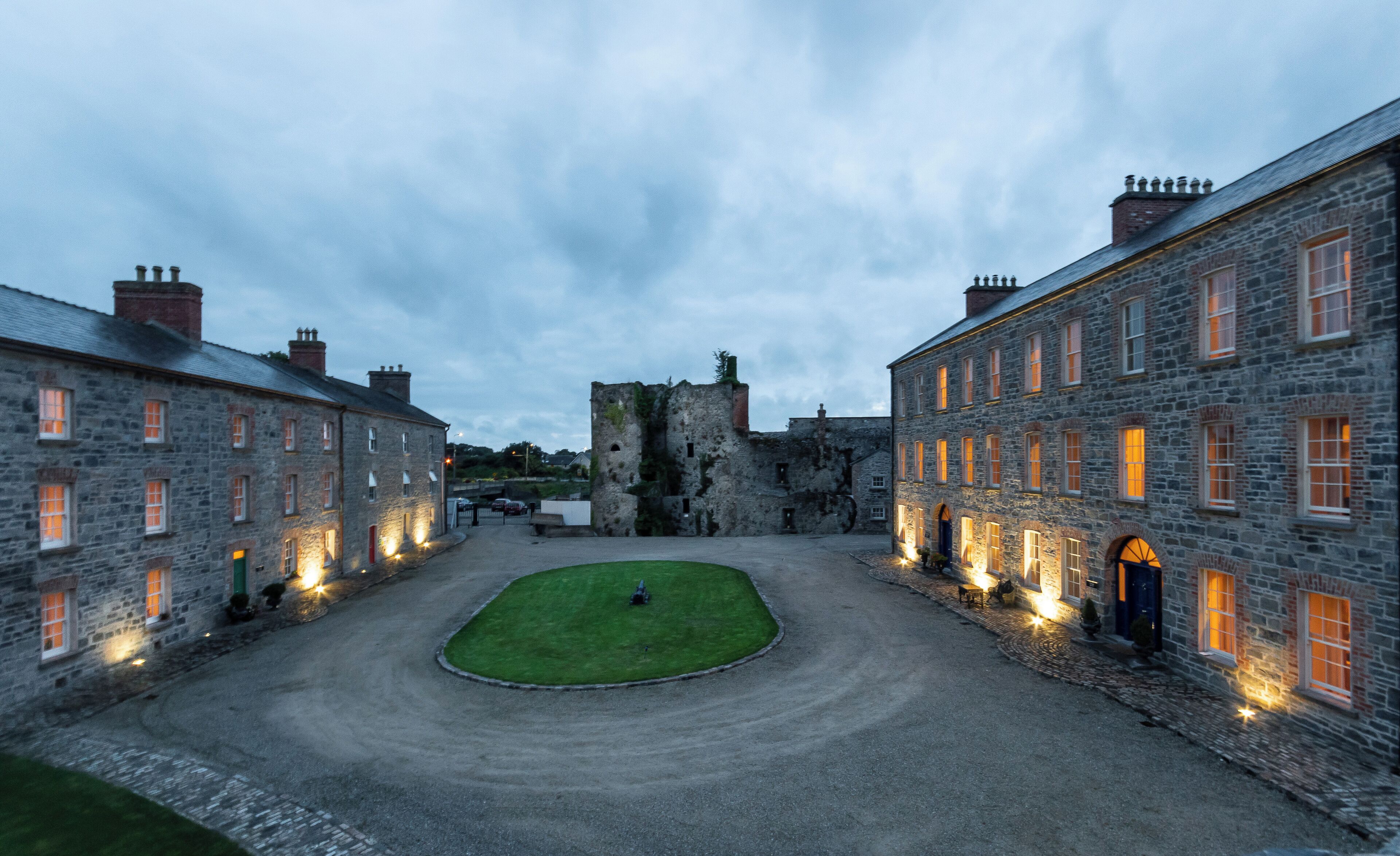 A courtyard with stone buildings, a grassy area, and a castle-like structure in the background.