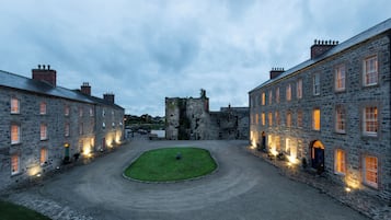 A courtyard with stone buildings, a grassy area, and a castle-like structure in the background.