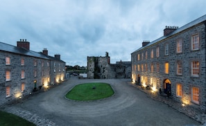 Ein Innenhof mit Steingebäuden, einer Rasenfläche und einer schlossähnlichen Struktur im Hintergrund.