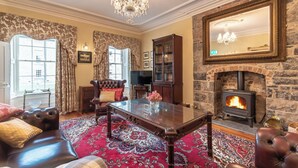 A traditional room with a fireplace, leather sofas, a large mirror, and a chandelier. - Beautifully Restored Soldier s Barracks to Sleep 10 People (Ennis)