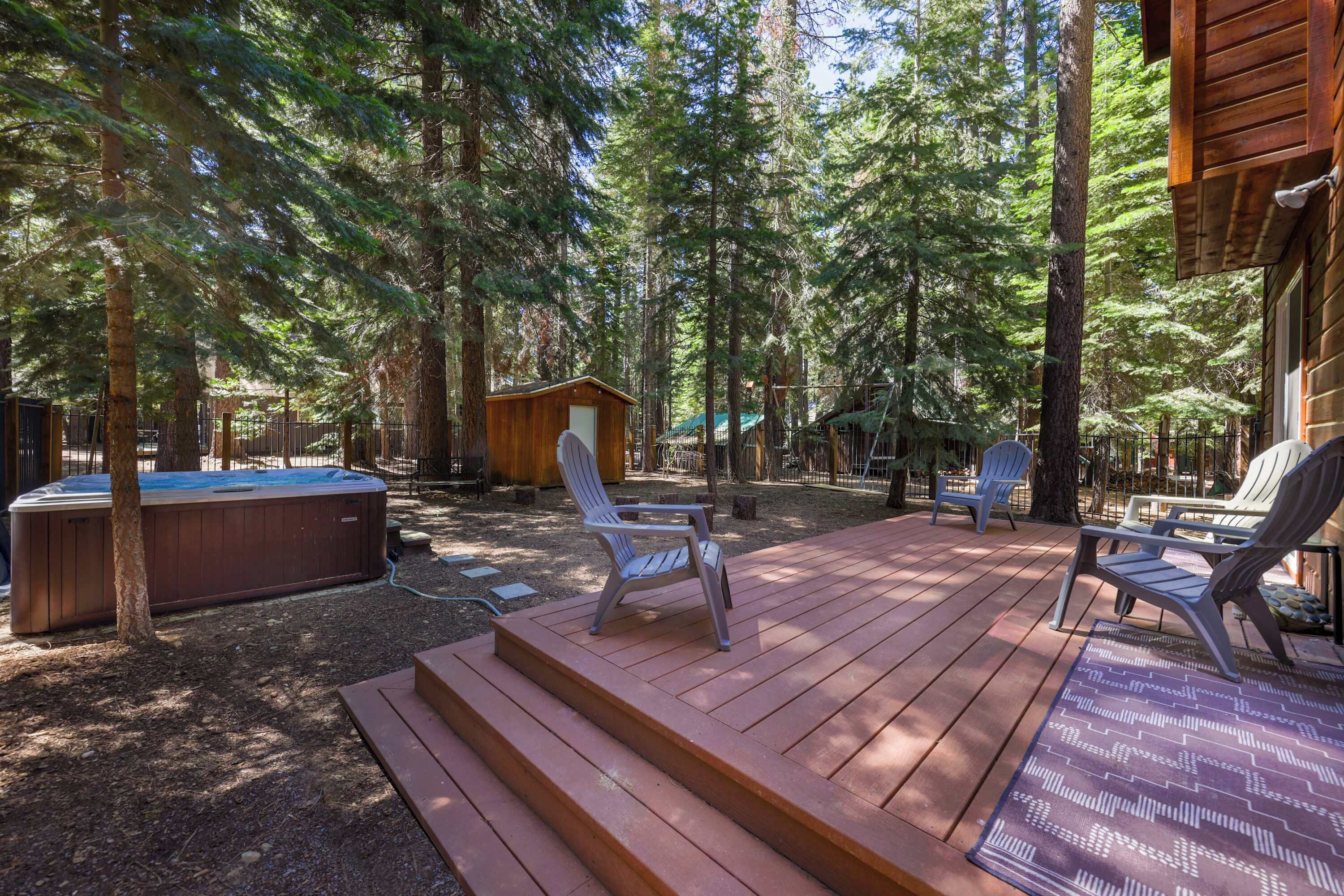 Una terraza de madera con mobiliario exterior y un jacuzzi en un área boscosa.