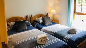 A hotel room with two beds, each with blue and white striped bedding, a wooden headboard, and a bedside table with a lamp.