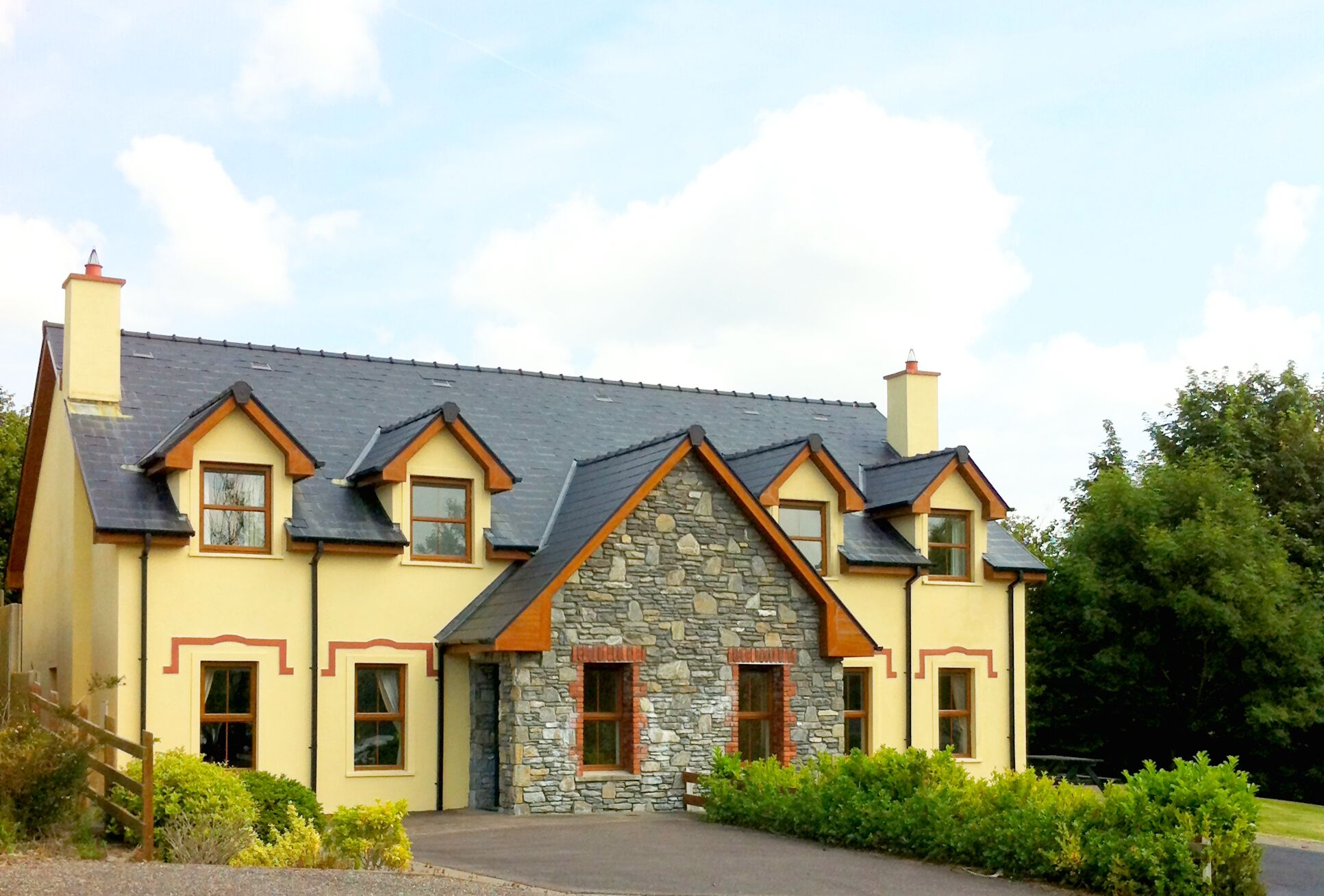 A two-story house with a stone facade, multiple chimneys, and a sloped roof.