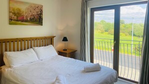 A hotel room with a bed, a nightstand, a lamp, a painting, and a balcony with a view of greenery. - Holiday Home Within Easy Walking Distance to Kenmare (Kenmare)