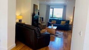 A modern living room with a dark leather sofa, a blue sofa, a wooden coffee table, and a painting on the wall. - Holiday Home Within Easy Walking Distance to Kenmare (Kenmare)