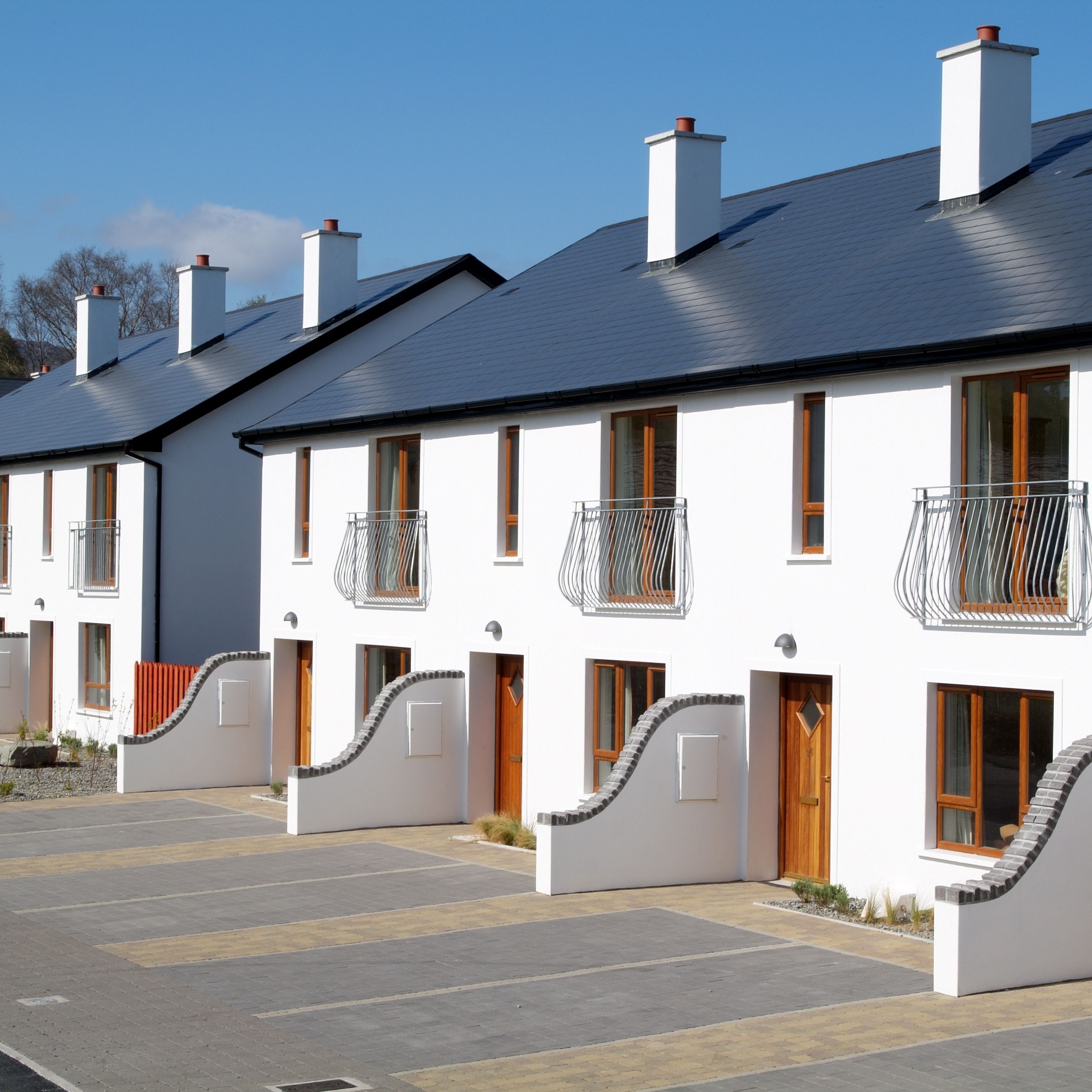 A row of modern, white buildings with dark roofs, each featuring a balcony with metal railings.