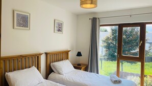 A bedroom with two beds, a bedside table with a lamp, and a window with curtains. - Holiday Home Within Easy Walking Distance to Kenmare (Kenmare)