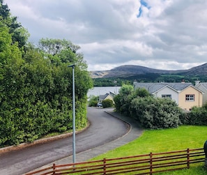 A curved road with a lamp post, surrounded by lush greenery and houses with grey roofs.