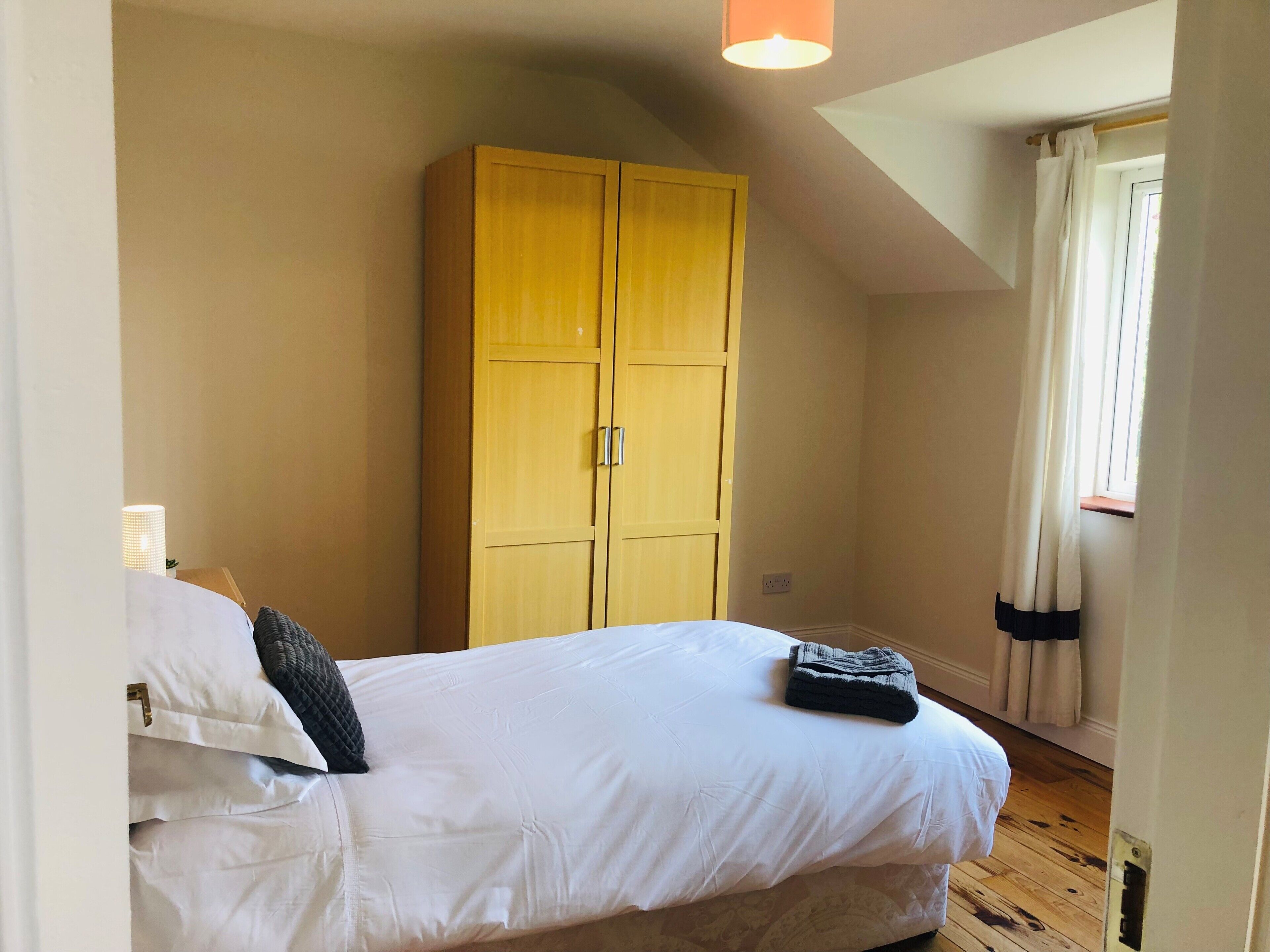A bedroom with a bed, a wardrobe, and a window with curtains.