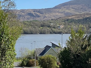 A lakeside view with a house in the foreground, a mountain in the background, and a clear sky.