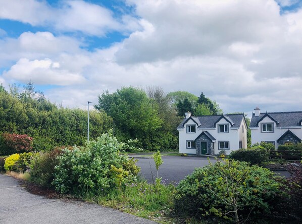 A row of white houses with dark roofs, surrounded by lush greenery and a clear sky.