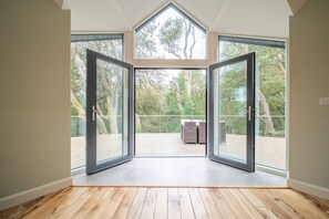 A room with a wooden floor, large glass doors leading to an outdoor area with a view of trees and a fenced garden. - Luxury 5 Bedroom Home With Outdoor Jacuzzi and Indoor Sauna (Gorteanish)