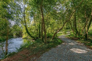 A gravel path leading through a forested area with a river on one side. - Luxury 5 Bedroom Home With Outdoor Jacuzzi and Indoor Sauna (Gorteanish)