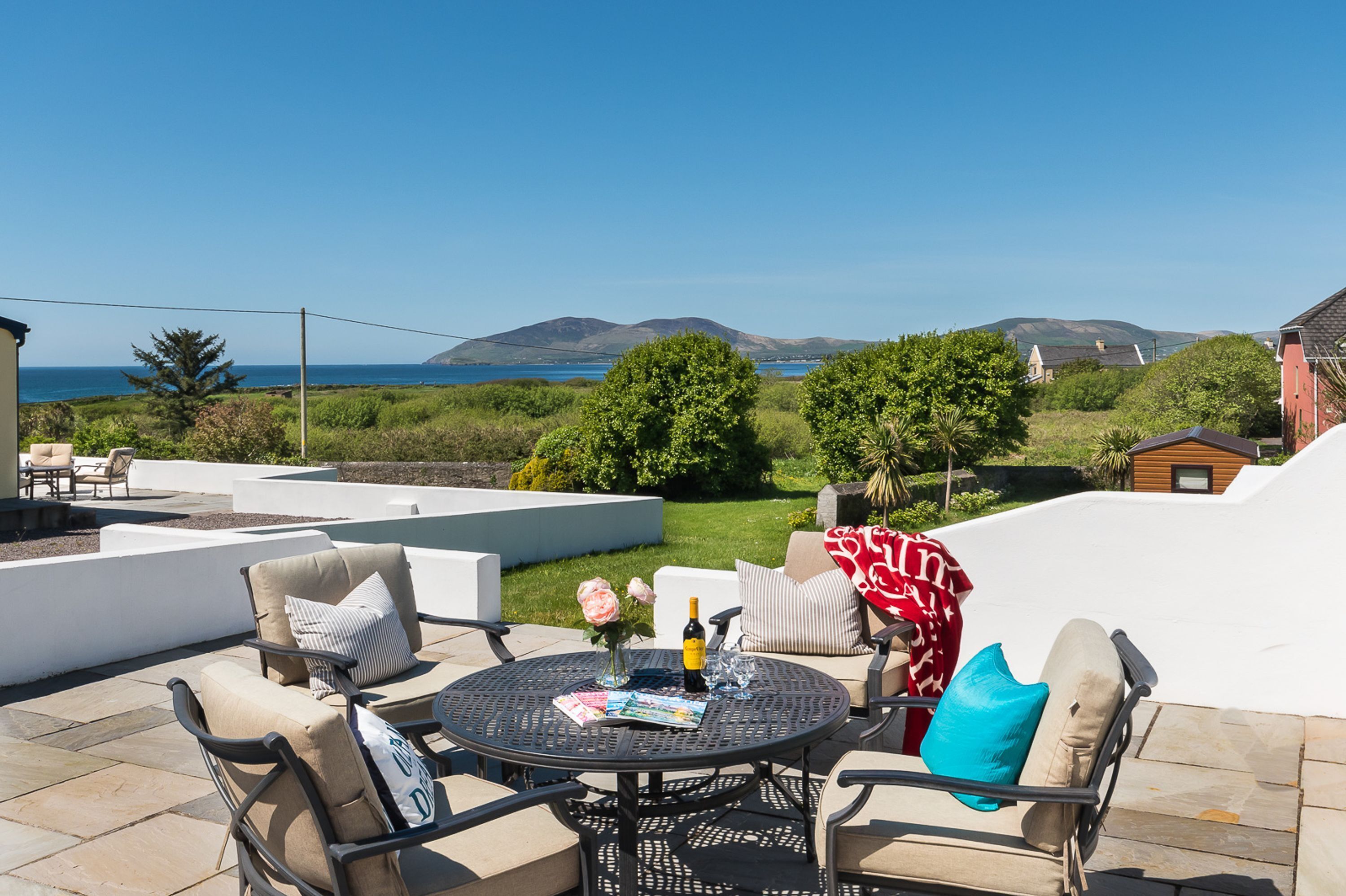 A patio with outdoor furniture, a round table, and a view of the sea and hills.