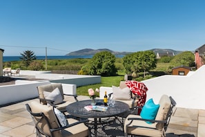 A patio with outdoor furniture, a round table, and a view of the sea and hills. - Large House With Adjoining Cottage Close to Waterville (Waterville)