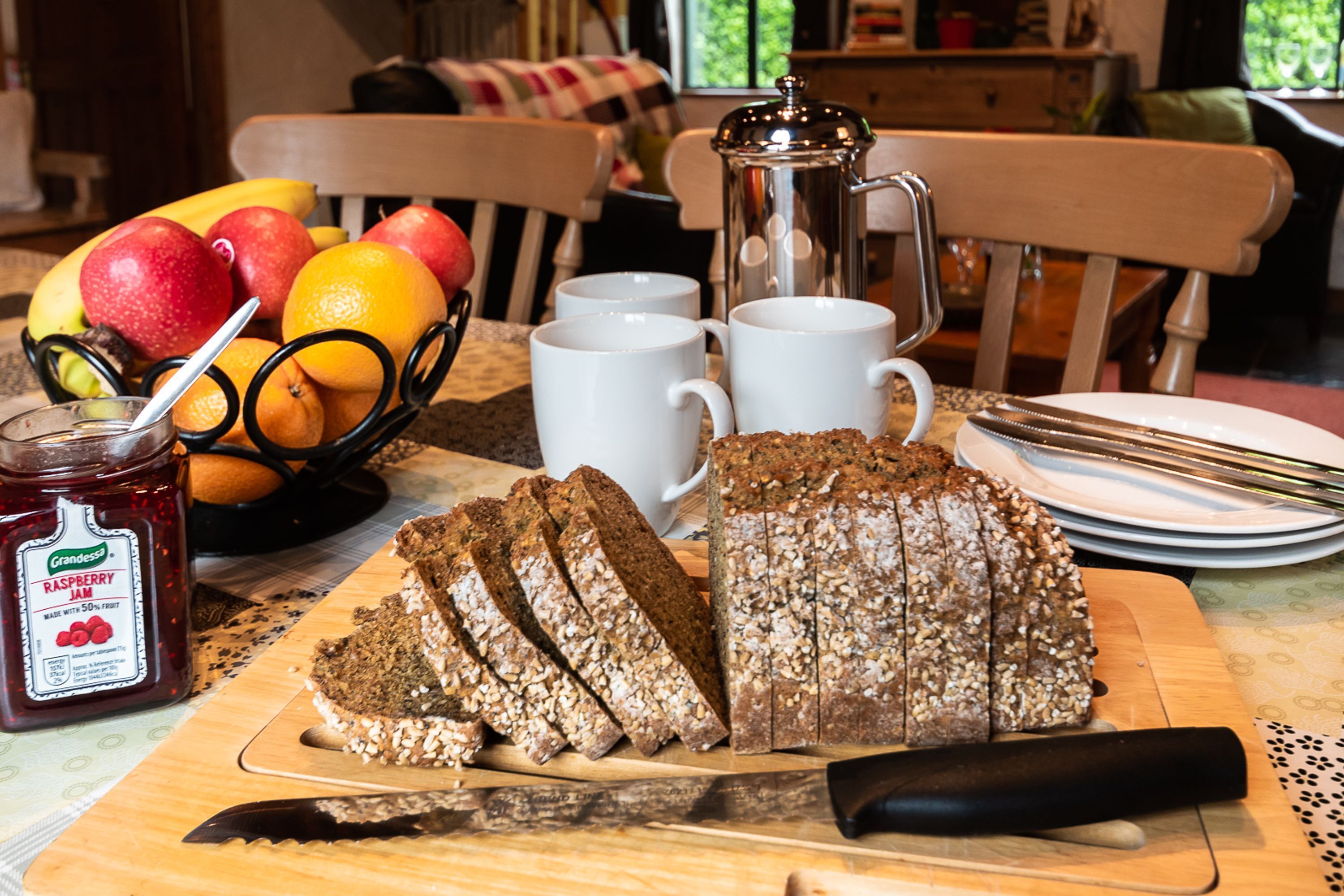 A breakfast table with sliced bread, a fruit bowl, and a coffee pot.