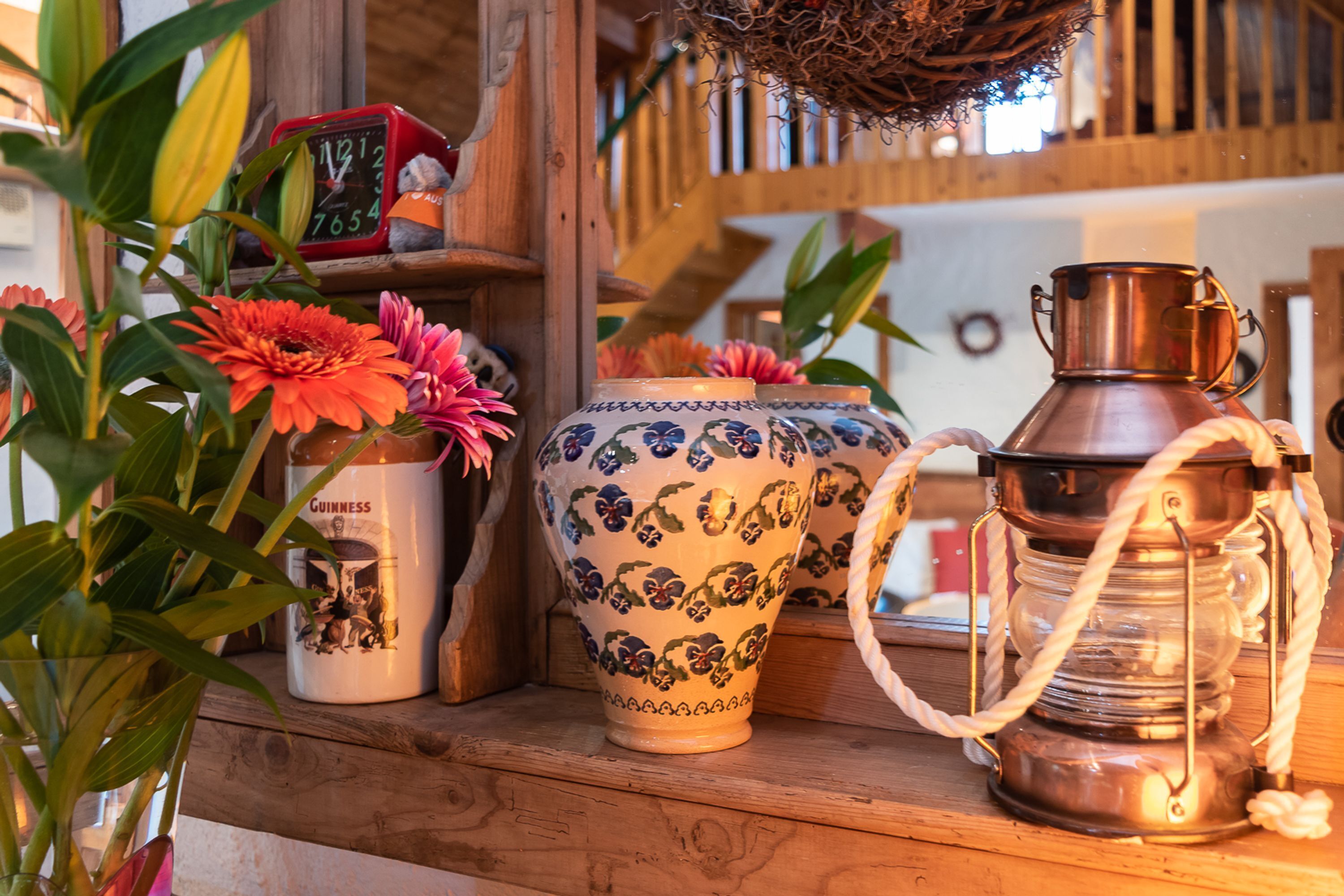 A wooden shelf with a decorative clock, a vase with flowers, and a lantern.