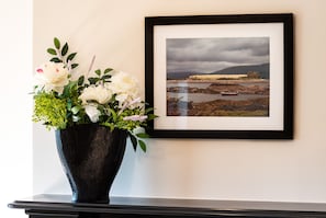 A framed landscape photograph on a wall, a black vase with white flowers, and a black table below. - 2 Bedroomed Home Just Steps From Kenmare Town (Kenmare)