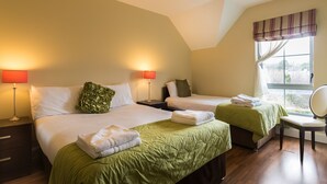Een hotelkamer met twee bedden, groen beddengoed, een raam met gordijnen en een stoel.