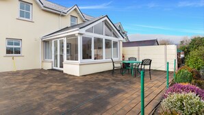 Une véranda avec un toit en verre, un espace patio avec une table et des chaises, et une terrasse en bois.