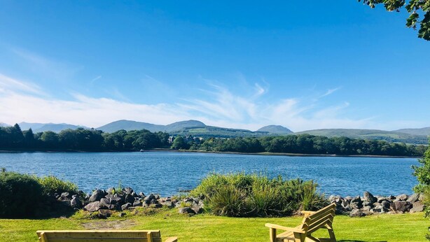 A lakeside view with two wooden benches facing the water, surrounded by grass and rocks.