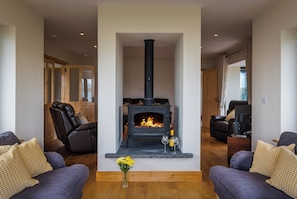 A living room with a central fireplace, two sofas, a coffee table, and a vase of flowers. - Luxury 4 Bedroom Holiday Home Overlooking the sea on Valentia Island (Valentia Island)