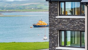 A coastal building with a stone facade and large windows overlooking a calm sea with a boat anchored nearby. - Luxury 4 Bedroom Holiday Home Overlooking the sea on Valentia Island (Valentia Island)