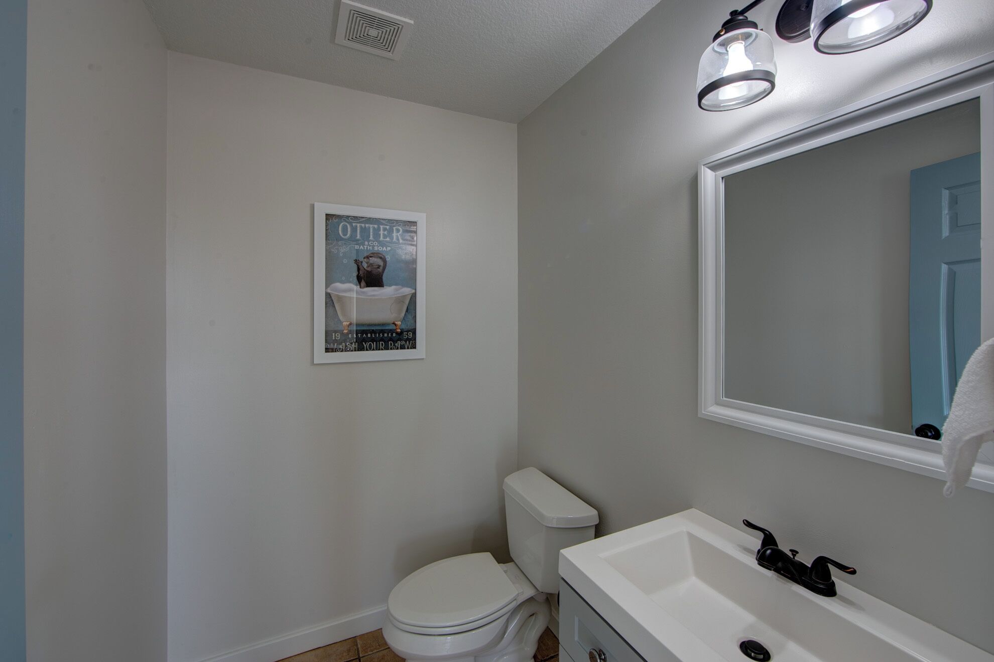 Une salle de bain équipée de toilettes, d’un lavabo, d’un miroir et d’une affiche ancienne accrochée au mur.