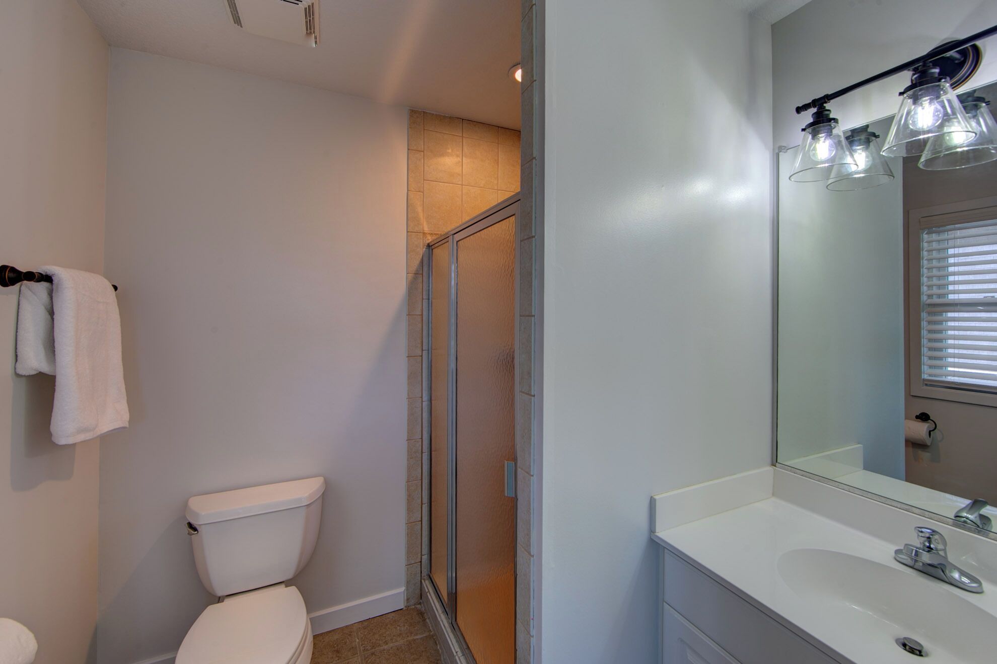 Un baño con inodoro, cabina de ducha de vidrio, lavamanos con espejo y toallero.