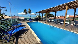 A pool area with blue lounge chairs, umbrellas, and a wooden deck. - Pousada Sandbeach (Trairi)