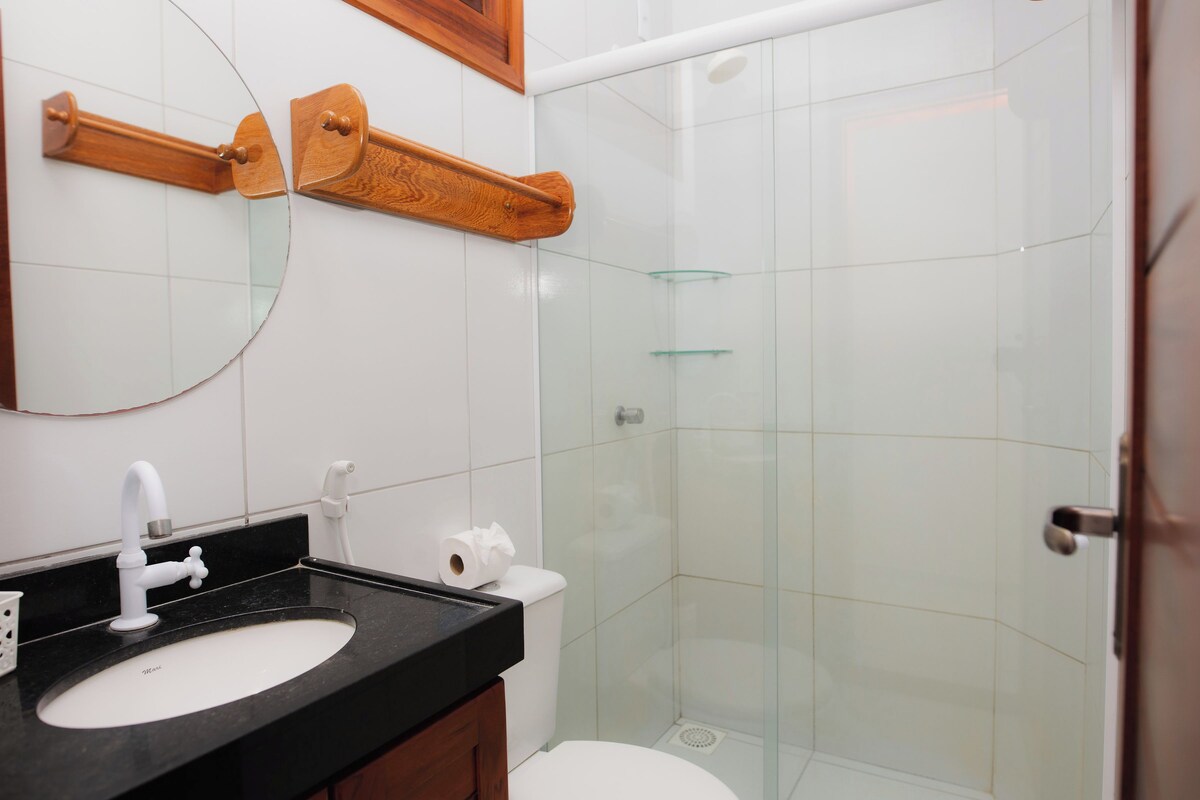 Un baño con lavamanos blanco, un espejo, inodoro y cabina de ducha con mampara de vidrio.