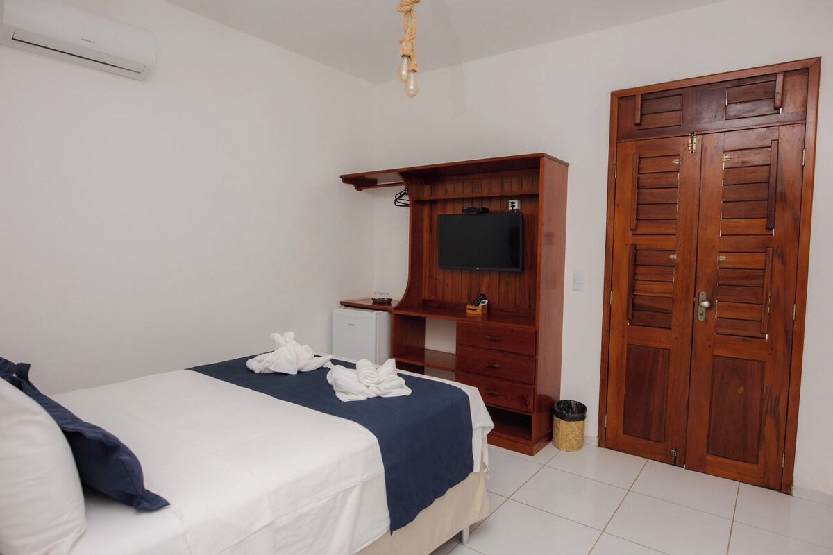 A hotel room with a bed, a wooden wardrobe, a television, and a small refrigerator.
